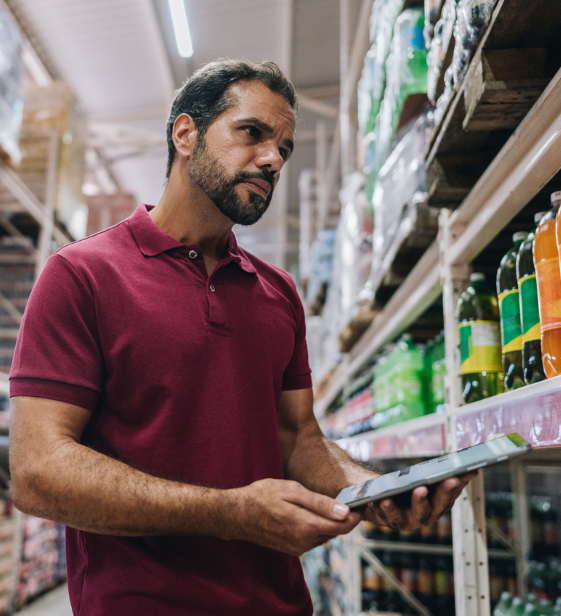 A frontline retail worker in a grocery store aisle uses a tablet to assess products, reflecting the challenges of supporting well-being in dispersed teams.